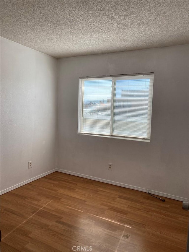 empty room with a textured ceiling, baseboards, and wood finished floors