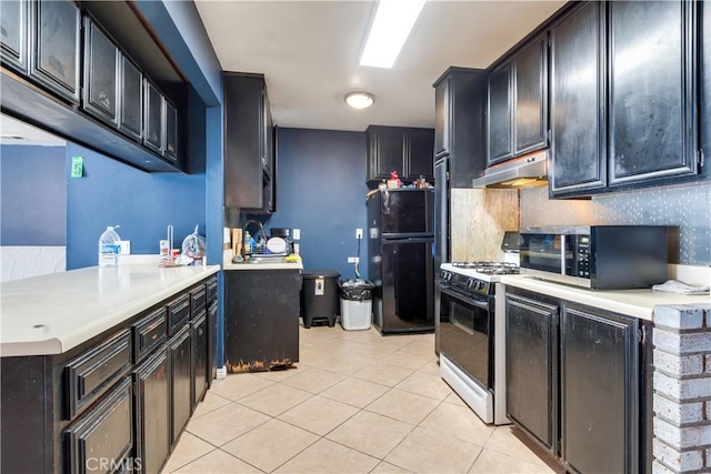 kitchen featuring light tile patterned floors, gas stove, freestanding refrigerator, under cabinet range hood, and stainless steel microwave