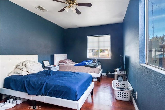 bedroom with wood finished floors, visible vents, baseboards, ceiling fan, and a textured wall