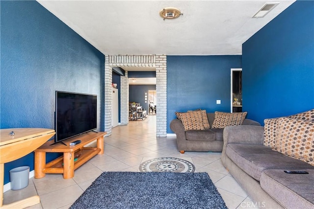 tiled living area featuring visible vents, brick wall, baseboards, and decorative columns