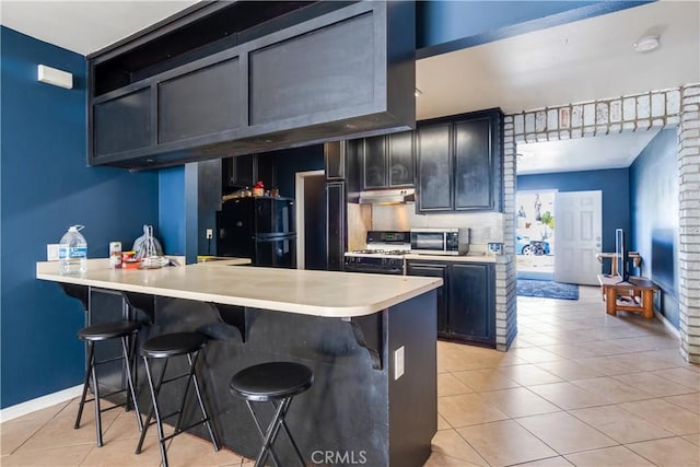 kitchen featuring light tile patterned floors, freestanding refrigerator, gas range oven, a kitchen bar, and stainless steel microwave