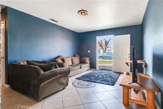 living area with light tile patterned flooring, a textured wall, visible vents, and baseboards