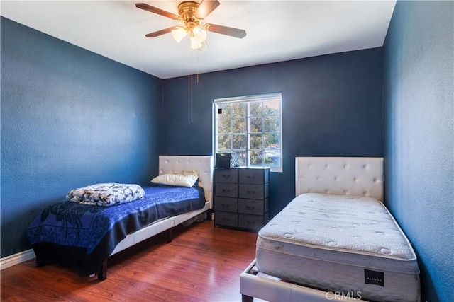 bedroom with a ceiling fan, wood finished floors, baseboards, and a textured wall