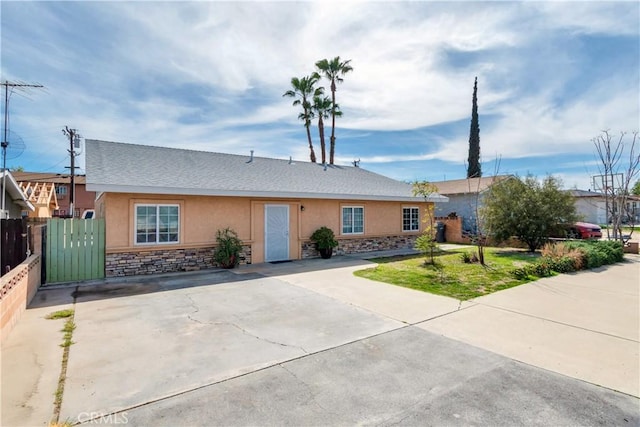 ranch-style house with stone siding, stucco siding, and fence