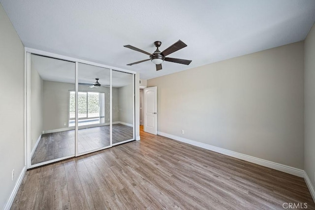 unfurnished bedroom featuring a closet, wood finished floors, a ceiling fan, and baseboards