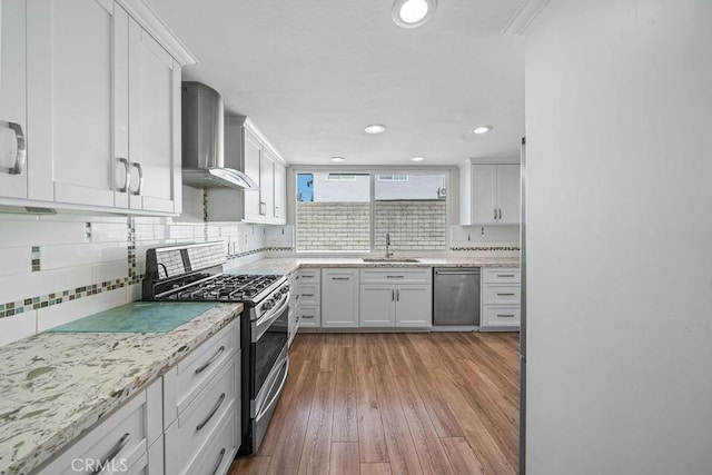 kitchen with wall chimney exhaust hood, appliances with stainless steel finishes, a sink, and white cabinetry