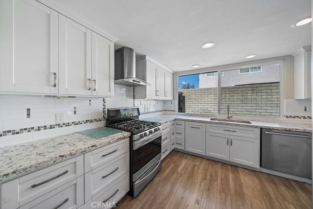 kitchen with dark wood-style floors, stainless steel appliances, decorative backsplash, a sink, and wall chimney exhaust hood