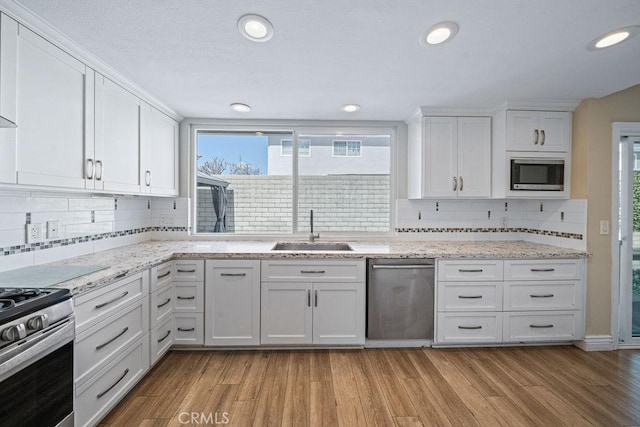 kitchen featuring light wood-type flooring, appliances with stainless steel finishes, white cabinets, and a sink