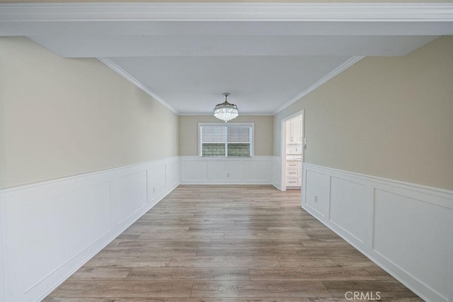 spare room with light wood finished floors, wainscoting, crown molding, and an inviting chandelier