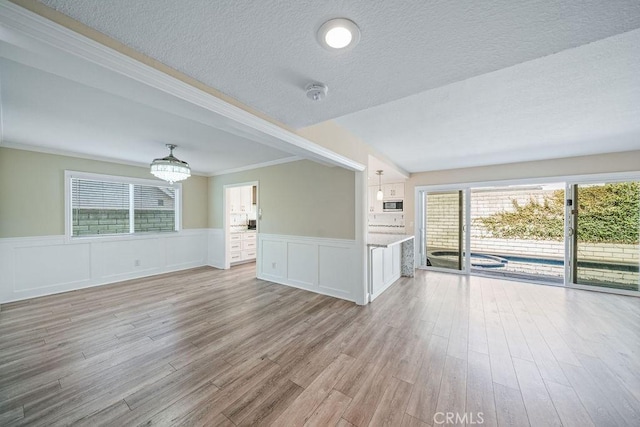 unfurnished living room with light wood-style flooring, ornamental molding, a textured ceiling, and wainscoting