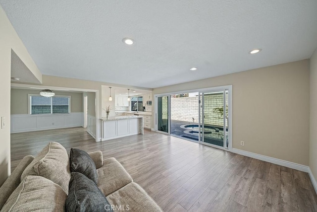 unfurnished living room featuring recessed lighting, wainscoting, a textured ceiling, light wood-type flooring, and baseboards