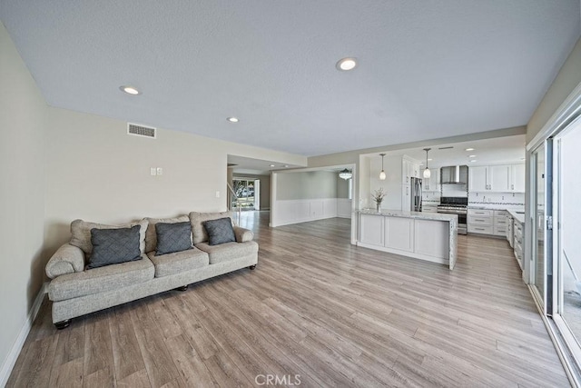 living room featuring a textured ceiling, light wood-style flooring, recessed lighting, a wainscoted wall, and visible vents