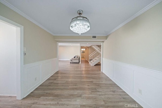 hall featuring crown molding, stairway, light wood-style flooring, and a notable chandelier