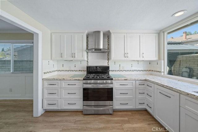 kitchen featuring white cabinetry, stainless steel gas range, decorative backsplash, wall chimney exhaust hood, and light wood finished floors