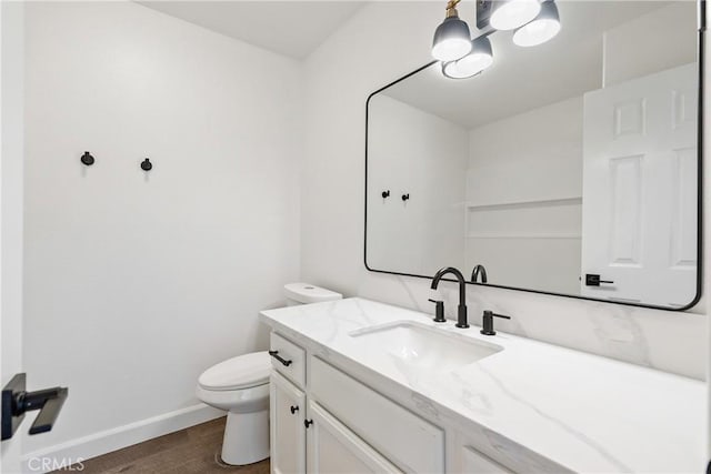 bathroom featuring toilet, baseboards, wood finished floors, and vanity