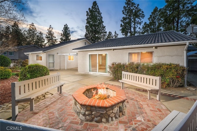 back of property at dusk with a tile roof, a fire pit, a patio, and stucco siding