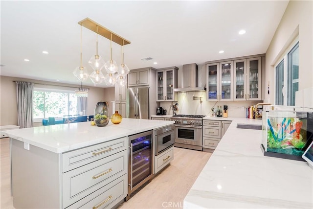 kitchen featuring wine cooler, light stone counters, stainless steel appliances, wall chimney exhaust hood, and a sink