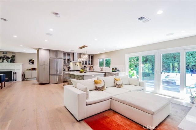 living area featuring visible vents, light wood finished floors, a premium fireplace, an inviting chandelier, and recessed lighting