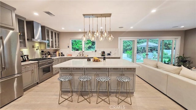 kitchen with visible vents, gray cabinetry, a sink, stainless steel appliances, and wall chimney range hood