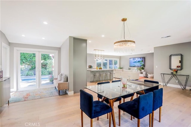 dining space with light wood-style flooring, a notable chandelier, and a wealth of natural light