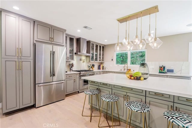 kitchen featuring high end appliances, visible vents, glass insert cabinets, decorative light fixtures, and wall chimney exhaust hood