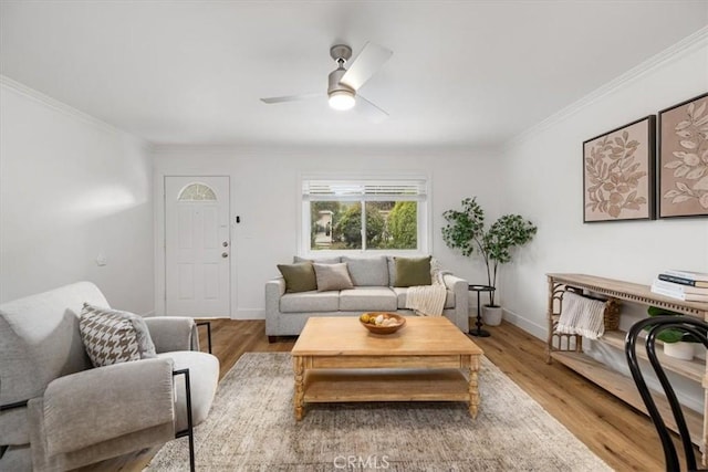 living area with baseboards, ceiling fan, wood finished floors, and crown molding