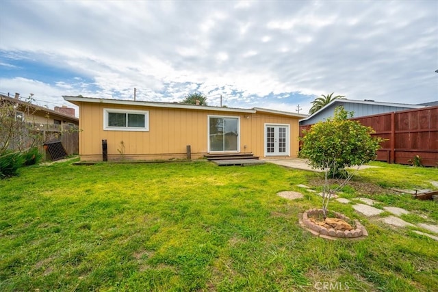 back of property with a yard, a fenced backyard, and french doors