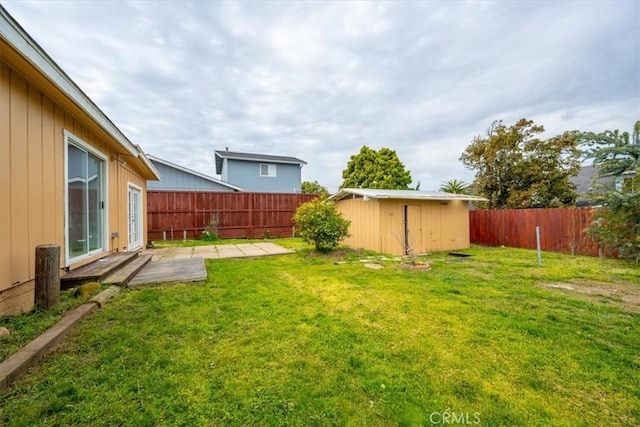 view of yard with a storage shed, a fenced backyard, a patio area, and an outbuilding