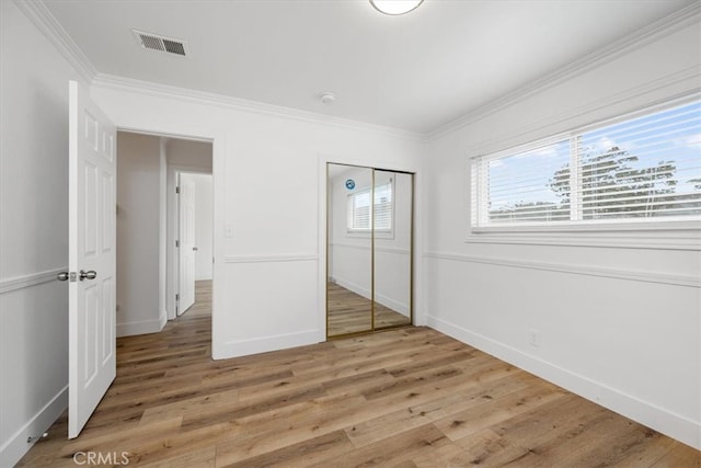 unfurnished bedroom with visible vents, baseboards, a closet, light wood-type flooring, and crown molding