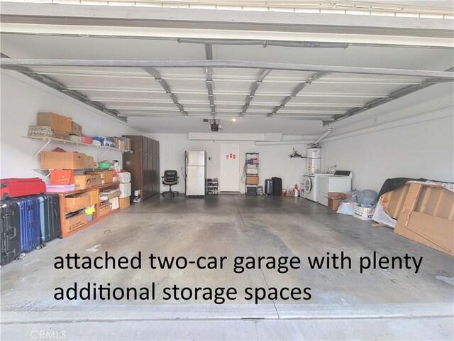 garage featuring water heater, separate washer and dryer, and freestanding refrigerator