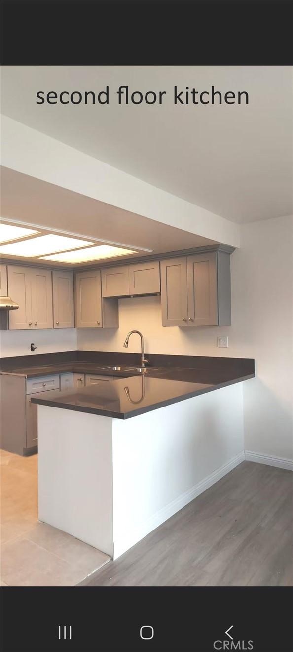 kitchen with baseboards, dark countertops, light wood-style flooring, gray cabinets, and a sink