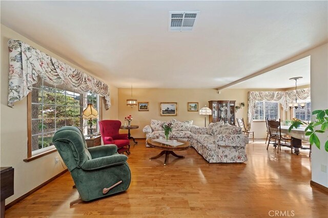 living room featuring wood finished floors, visible vents, baseboards, beam ceiling, and an inviting chandelier