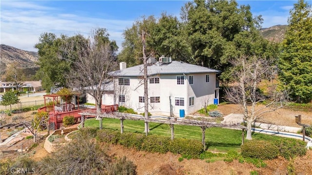 back of house featuring a deck with mountain view, a yard, a chimney, and stucco siding