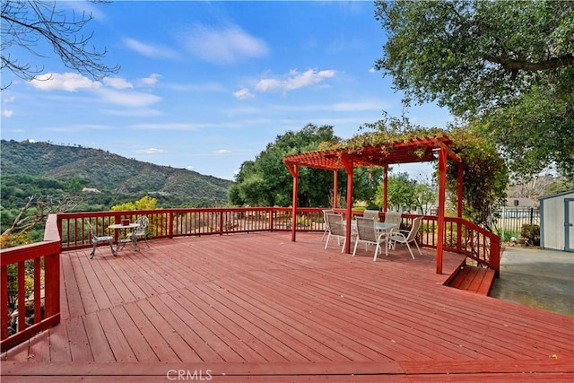 wooden terrace featuring outdoor dining space, a mountain view, an outbuilding, and a pergola