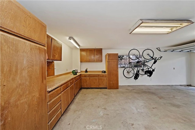 kitchen with brown cabinetry, light countertops, and unfinished concrete flooring