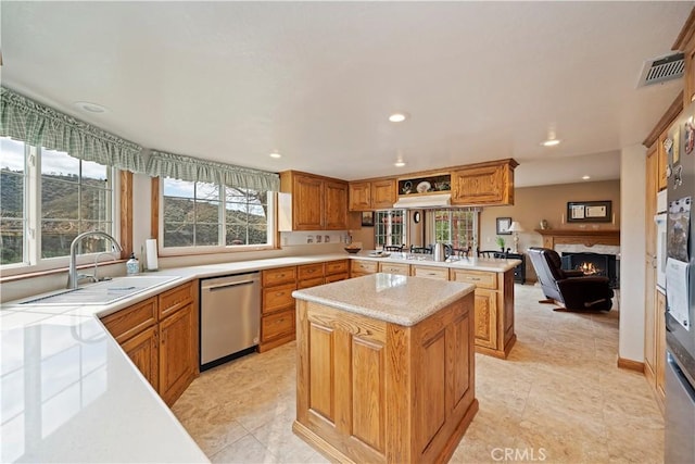 kitchen featuring a warm lit fireplace, a peninsula, a sink, visible vents, and stainless steel dishwasher