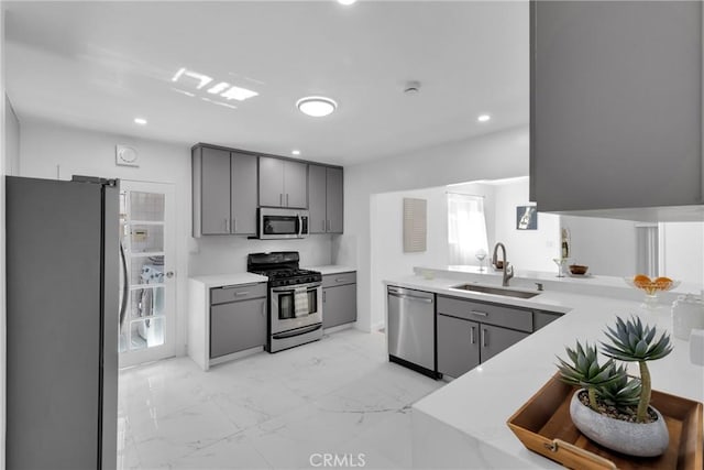 kitchen with a sink, marble finish floor, appliances with stainless steel finishes, and gray cabinetry