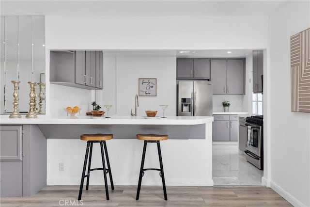 kitchen featuring gray cabinetry, stainless steel appliances, a peninsula, a breakfast bar area, and light countertops