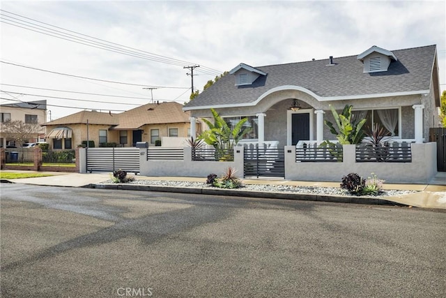 view of front facade featuring a gate, a fenced front yard, roof with shingles, and stucco siding