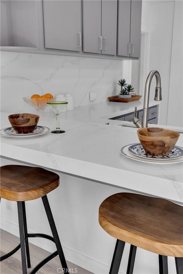 kitchen featuring a breakfast bar area, light stone counters, tasteful backsplash, and gray cabinetry