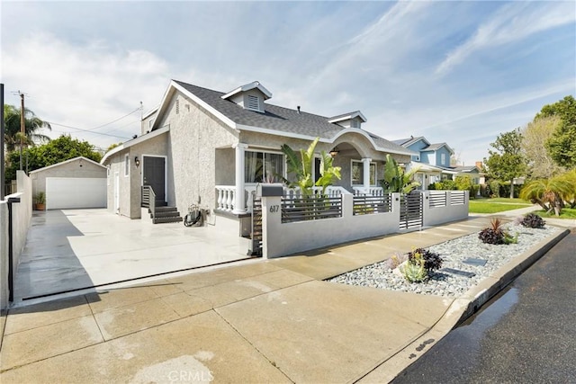 view of front facade with a detached garage, a fenced front yard, concrete driveway, stucco siding, and an outdoor structure