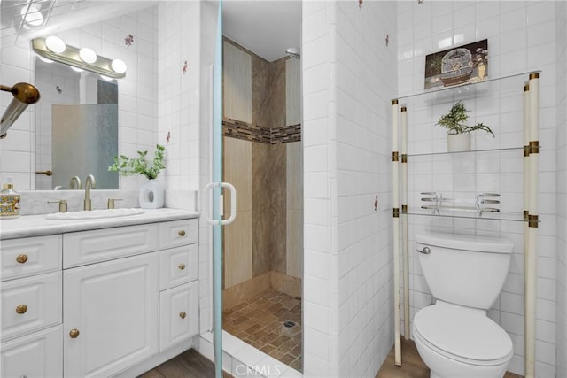 bathroom with toilet, tile walls, a stall shower, and vanity