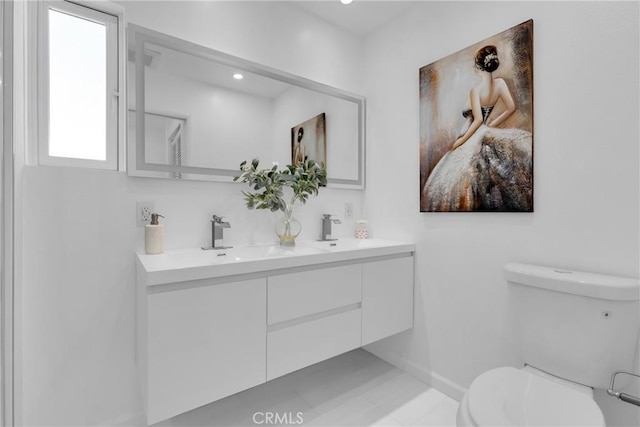 bathroom featuring double vanity, toilet, baseboards, and a sink