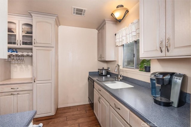 kitchen featuring a sink, visible vents, dark countertops, dark wood finished floors, and glass insert cabinets