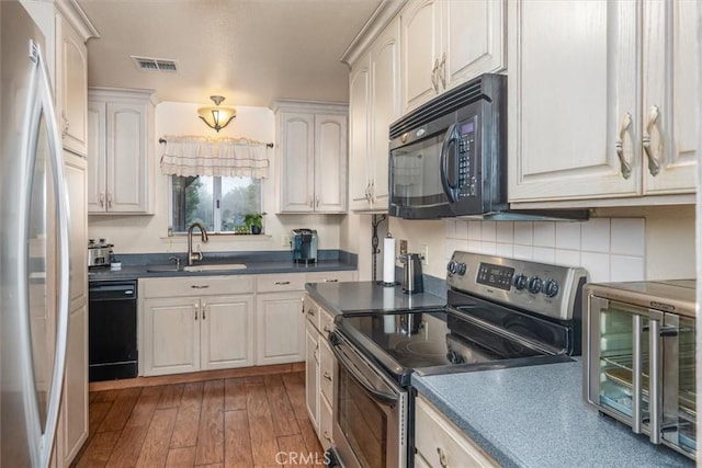 kitchen featuring wood finished floors, a sink, visible vents, decorative backsplash, and black appliances