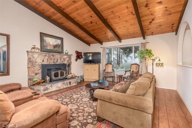 living area featuring vaulted ceiling with beams, wood-type flooring, wood ceiling, a wood stove, and baseboards