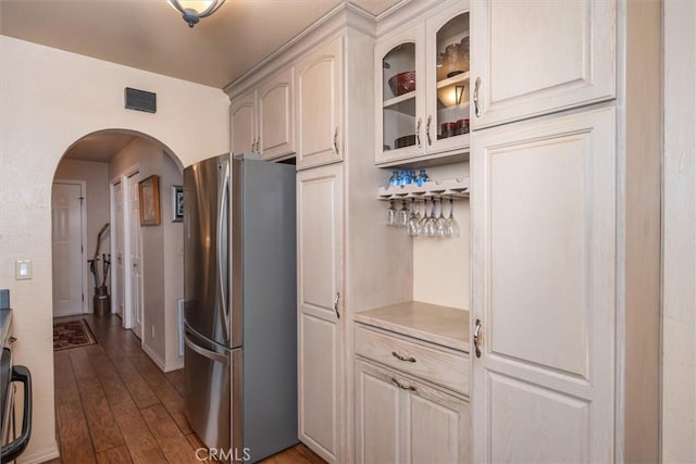 kitchen featuring arched walkways, light countertops, glass insert cabinets, freestanding refrigerator, and dark wood-type flooring