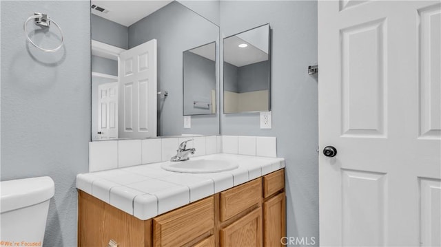 bathroom featuring toilet, vanity, and visible vents