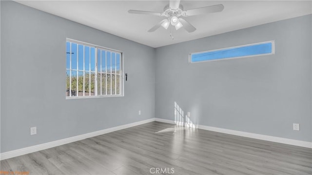 empty room with wood finished floors, a ceiling fan, and baseboards