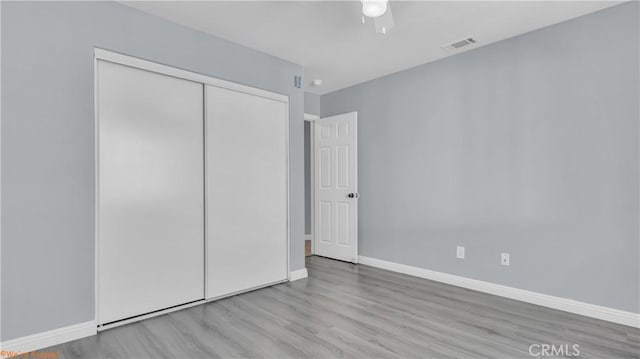 unfurnished bedroom with ceiling fan, wood finished floors, visible vents, baseboards, and a closet